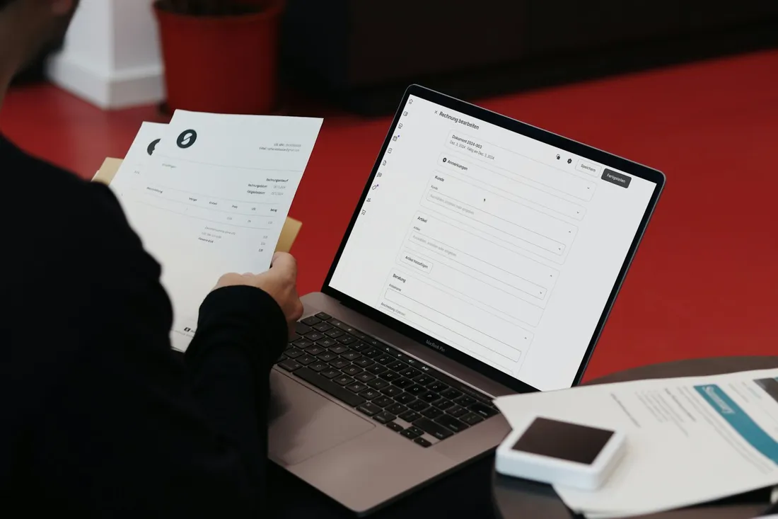 Paper invoices being typed into a billing form on a laptop